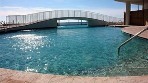 Ein klares, blaues Schwimmbecken mit einer Brücke, einem Poolbereich und einem Gebäude mit einer gewölbten Dachform.