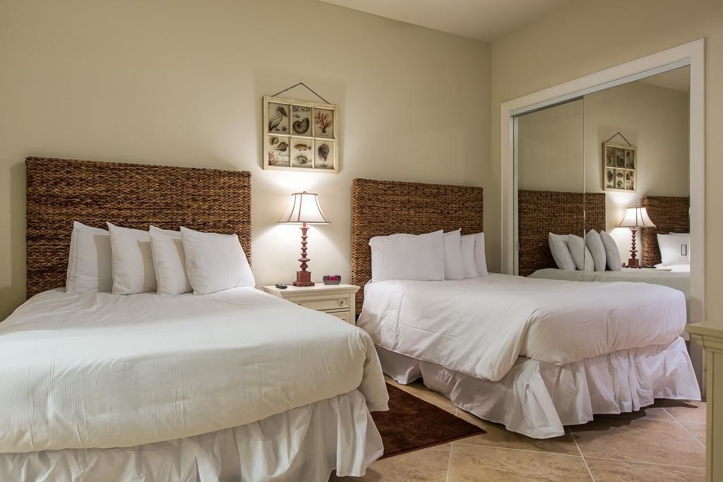 A hotel room with two beds, a nightstand with a lamp, a framed picture on the wall, and a large mirror.