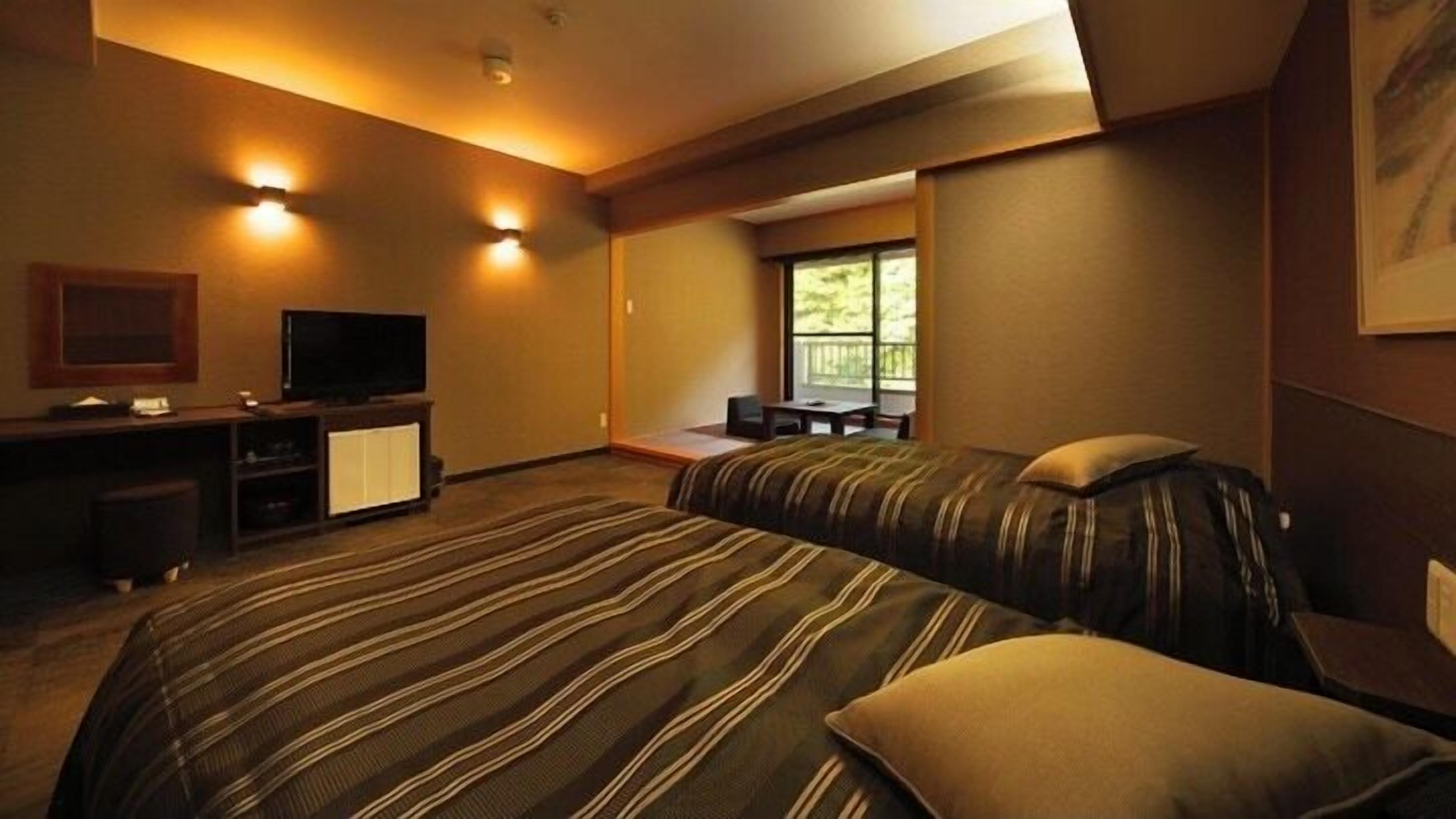 Quarto de hotel com duas camas, televisão, escrivaninha e janela com vista para árvores.