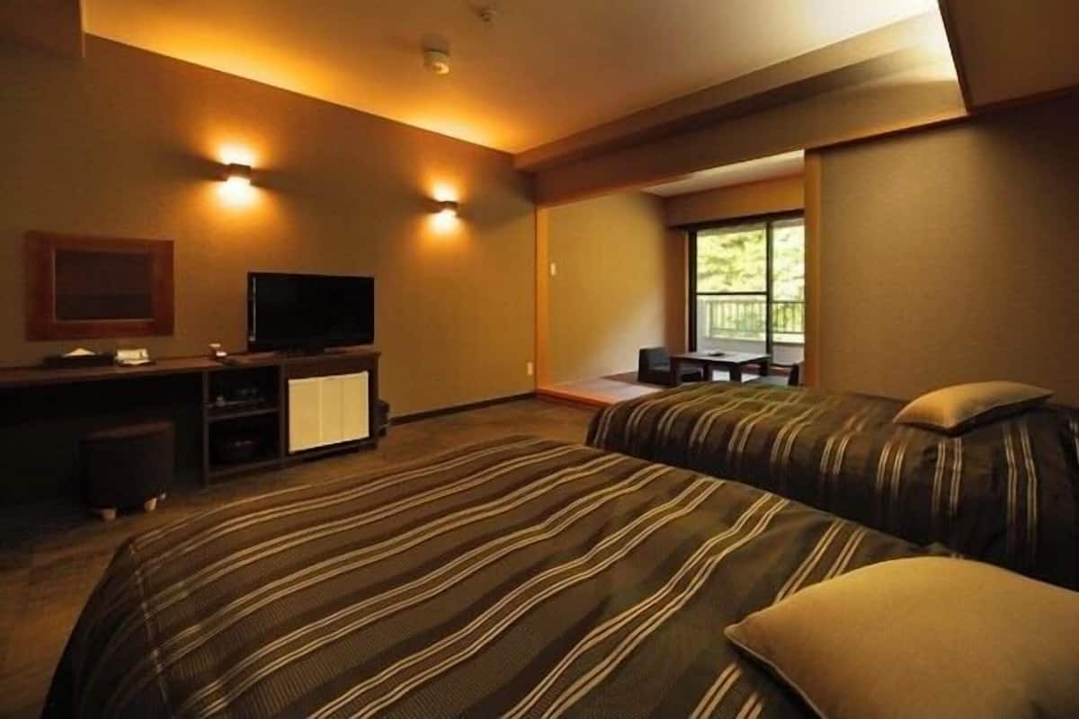Ett hotellrum med två sängar, en tv, ett skrivbord och ett fönster med utsikt över träd.
