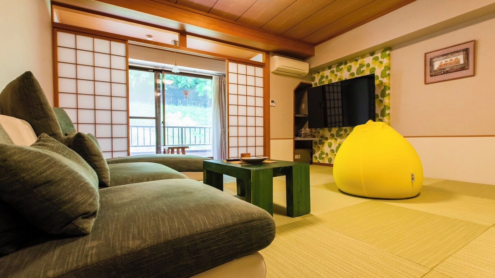 Een traditionele Japanse kamer met tatami vloerbedekking, een lage tafel, een bank en een gele relaxfauteuil.