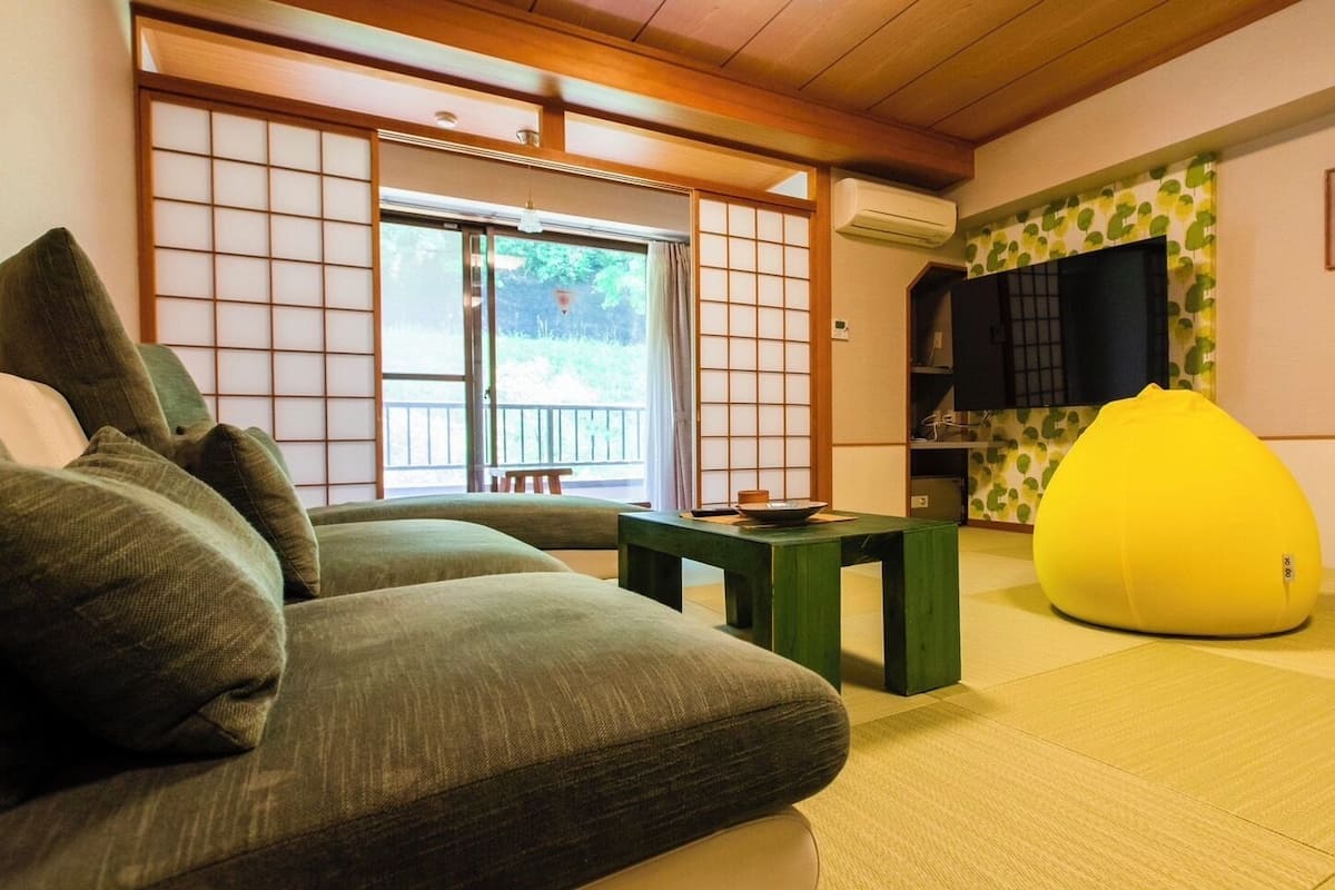 Ett traditionellt japanskt rum med tatamimattor på golvet, ett lågt bord, en soffa och en gul sittpuff.
