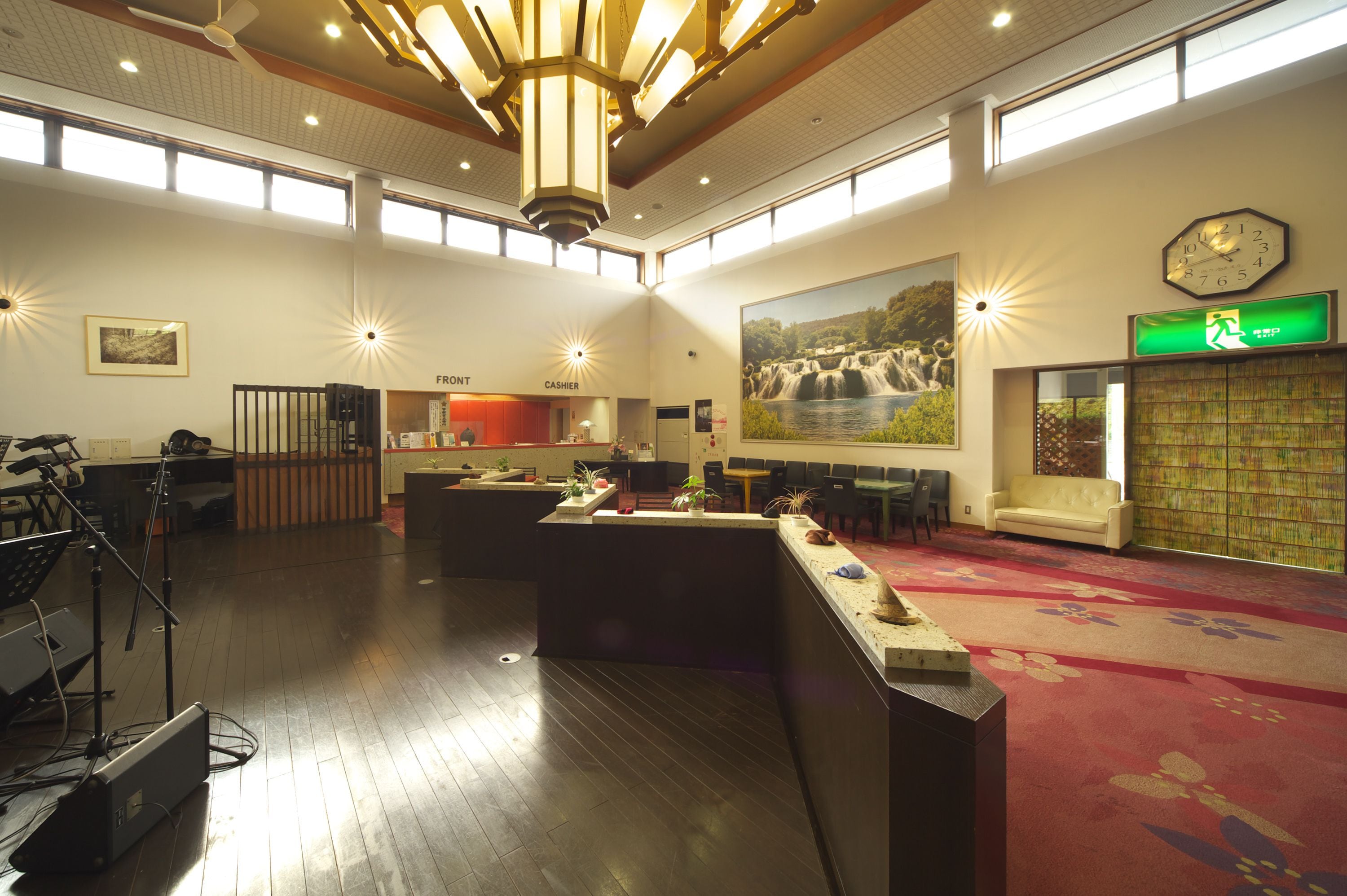 A spacious lobby with a reception desk, a cashier area, a seating area with a sofa, and a large wall-mounted clock.