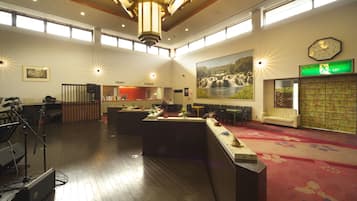 A spacious lobby with a reception desk, a cashier area, a seating area with a sofa, and a large wall-mounted clock.