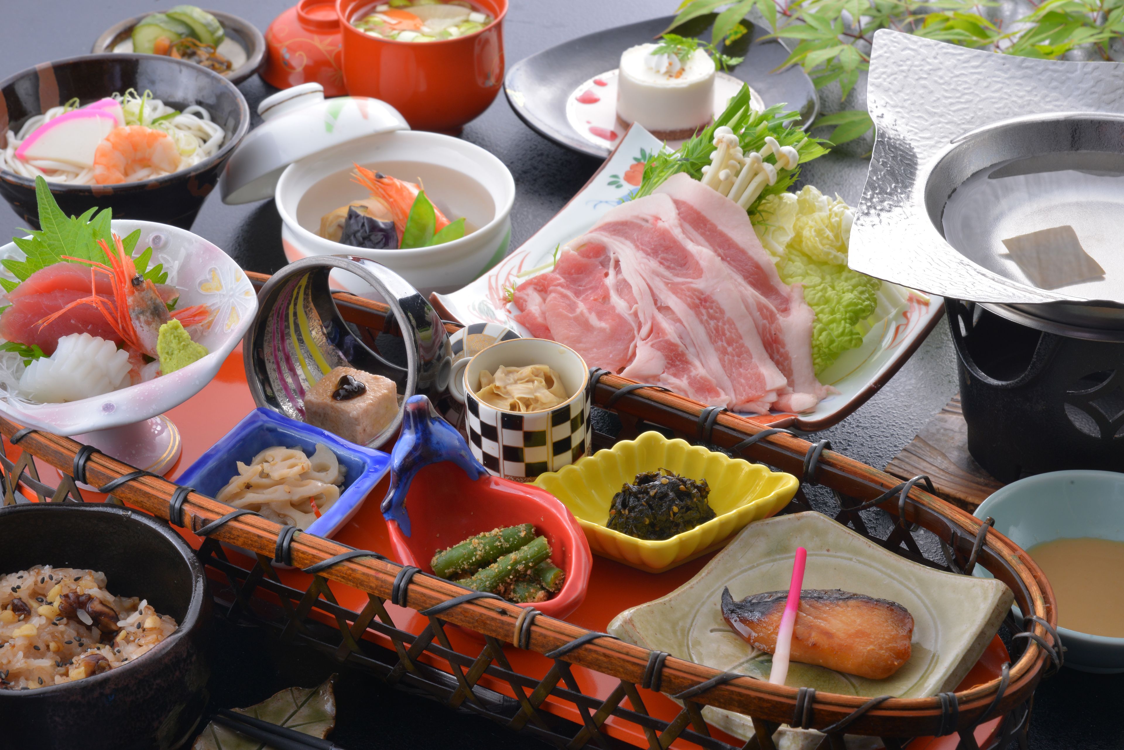A variety of dishes and food items arranged on a table, including bowls, plates, and a hot pot.