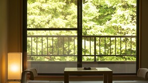 A room with tatami mats, a low table, and a view of lush greenery through large windows.