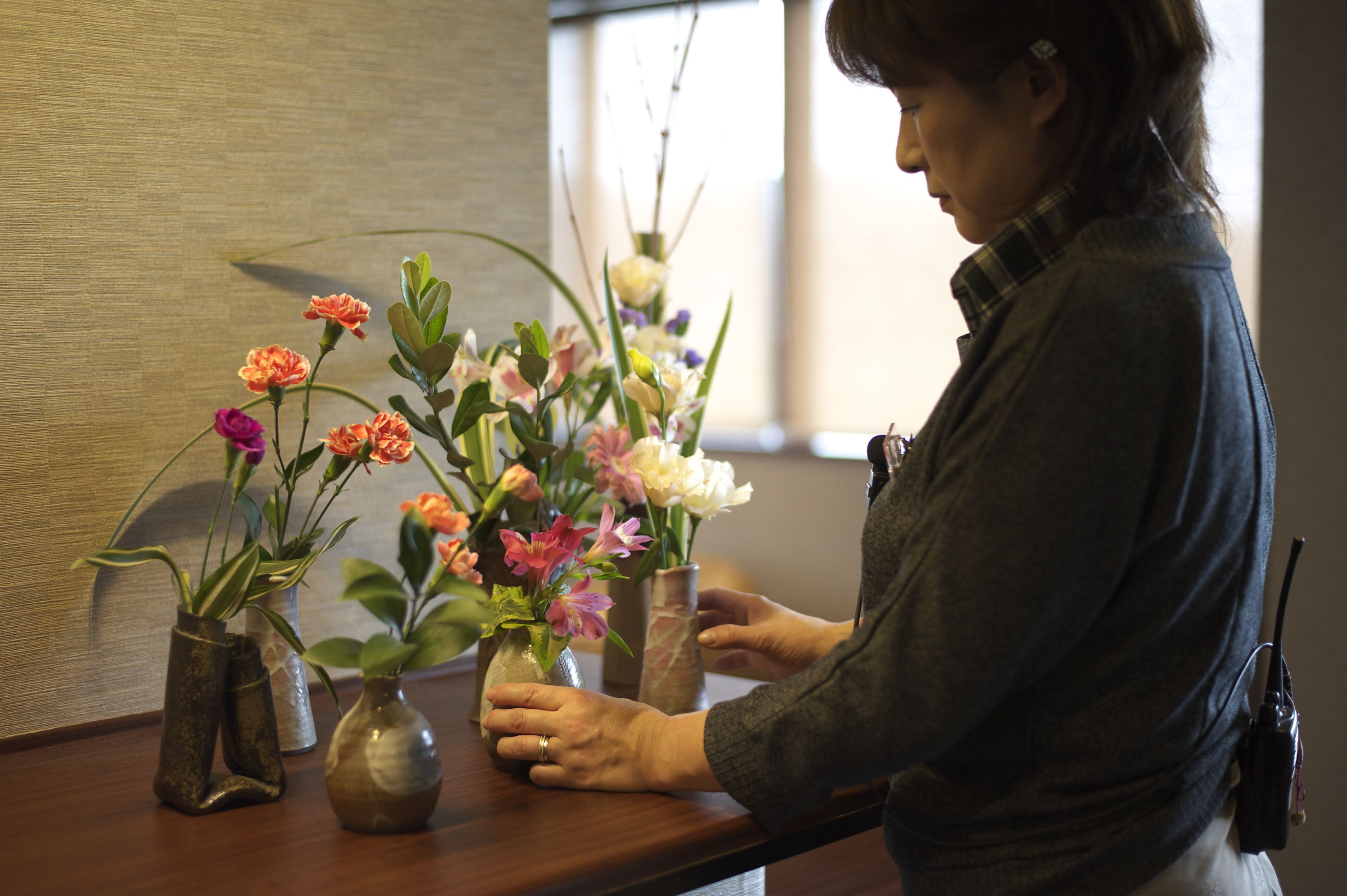 A person arranging flowers in vases on a wooden table.