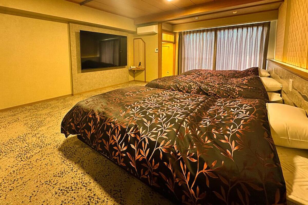 A hotel room with a large bed, a TV, and a window with curtains.