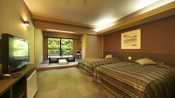 A hotel room with two beds, a TV, a desk with a computer, and a window with a view of greenery.