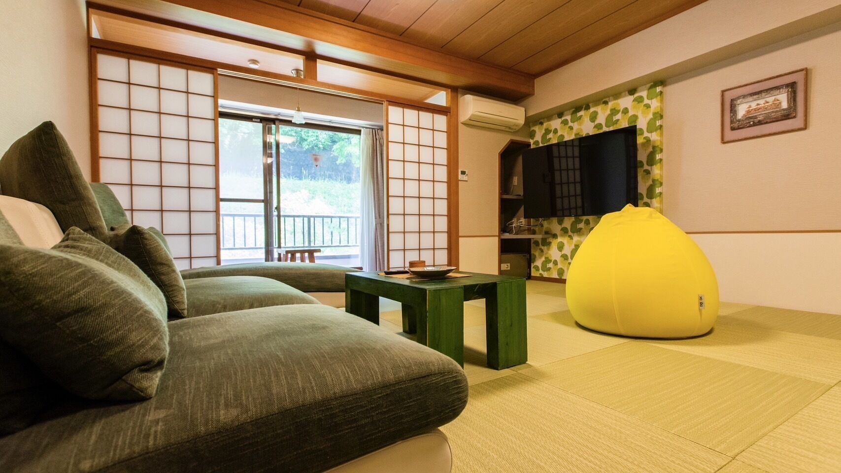 Een traditionele Japanse kamer met tatami vloeren, een lage tafel, een groene bank en een gele relaxstoel.