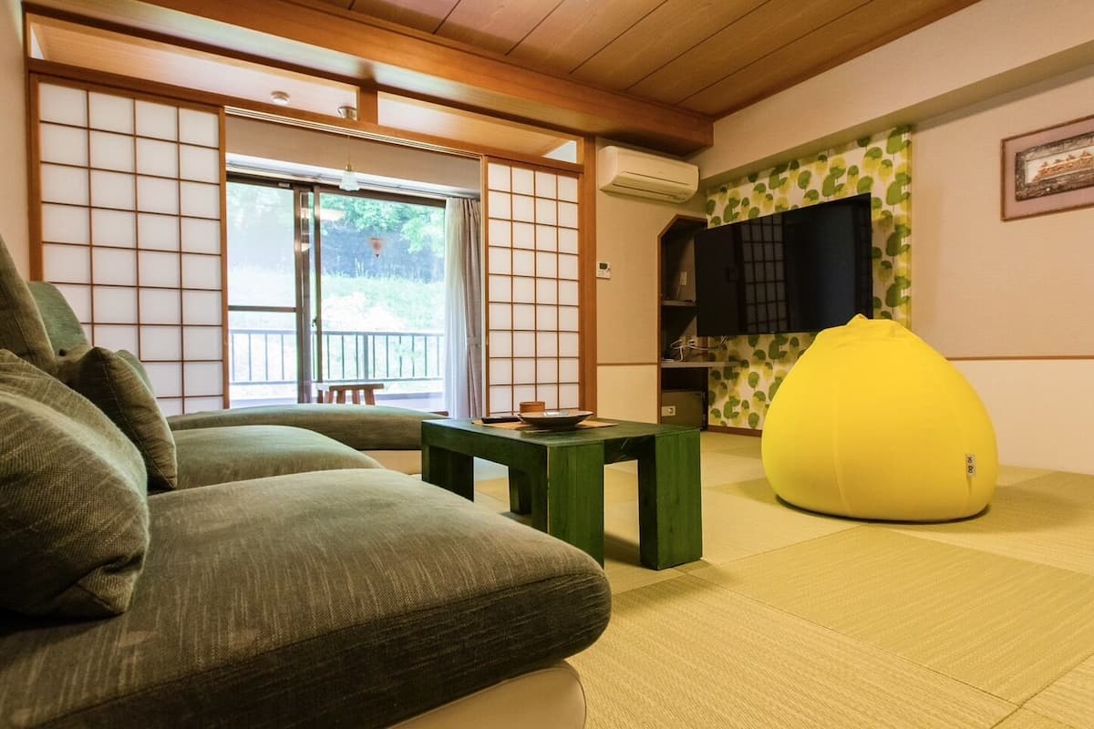 A traditional Japanese room with tatami flooring, a low table, a green sofa, and a yellow bean bag.