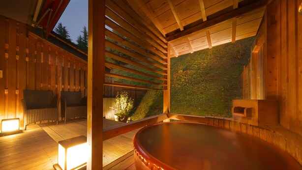 A wooden spa area with a hot tub, seating, and a view of a green hillside.