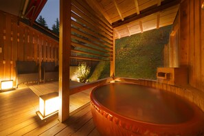 Et træspaområde med jacuzzi, siddepladser og udsigt til en grøn bakke.