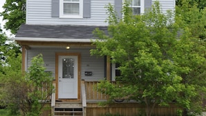 A two-story house with a front porch, a wooden fence, and a small front yard. - Moncton Suites - 81 Maple Street (Moncton)