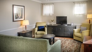 A living room with a sofa, two armchairs, a coffee table, a TV, a cabinet, and a ceiling fan. - Moncton Suites - 267 Universite Ave (Moncton)