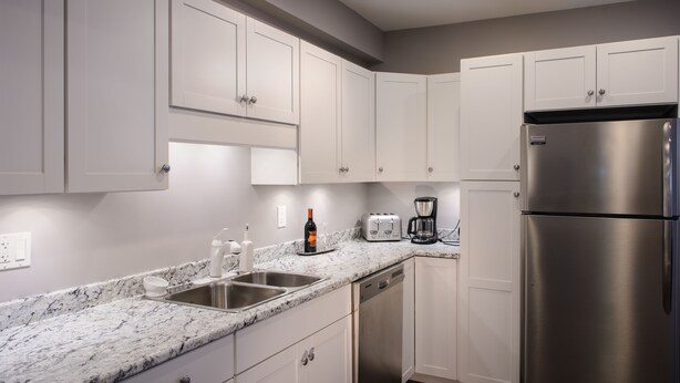 A modern kitchen with white cabinets, a stainless steel refrigerator, a coffee maker, and a toaster. - Moncton Suites - 267 Universite Ave (Moncton)