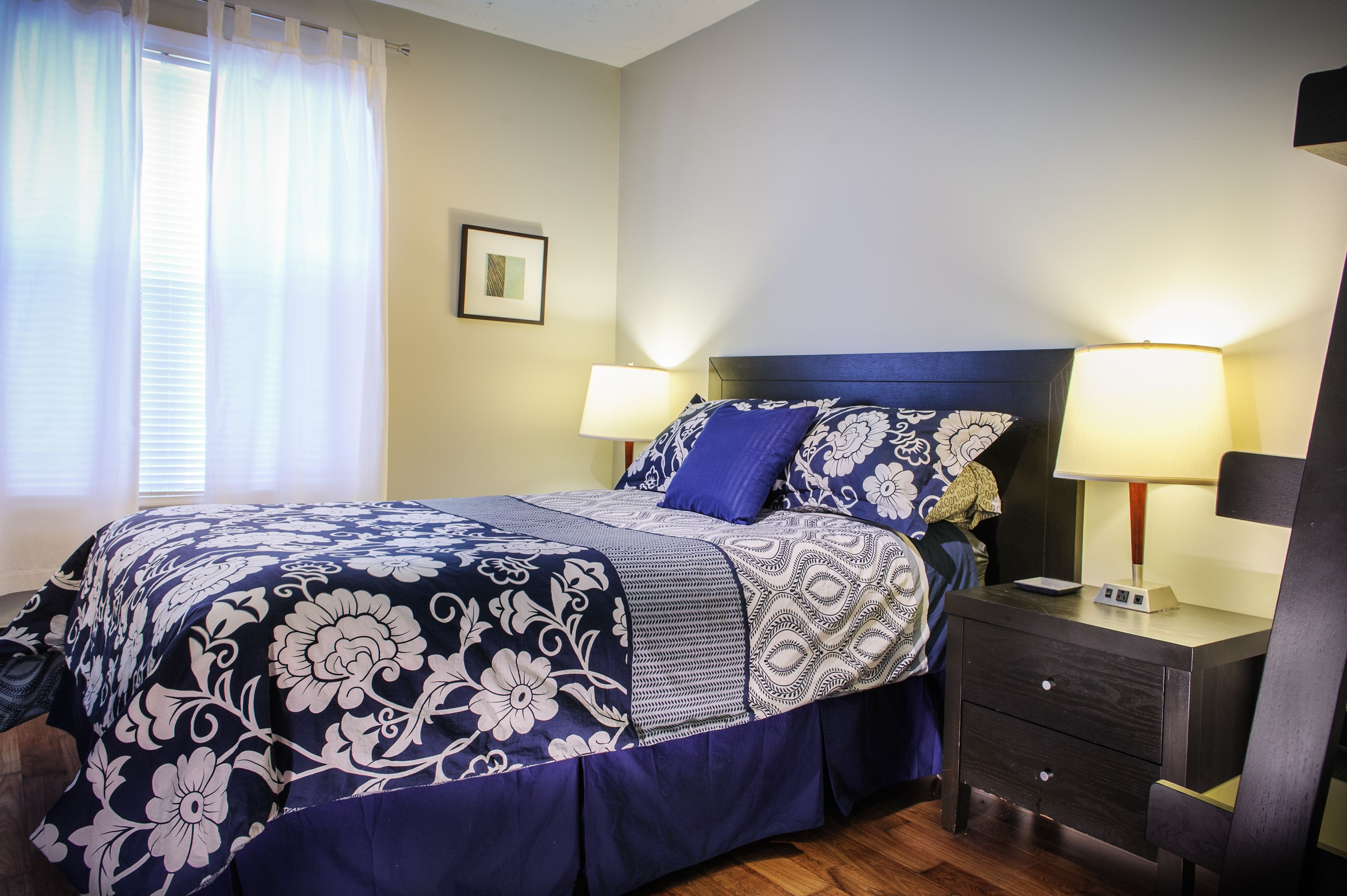 A neatly made bed with floral bedding, two bedside lamps, and a nightstand with a clock.