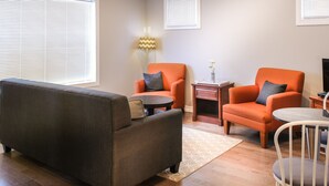 A living room with a grey sofa, two orange armchairs, a small round table, and a white chair. - Moncton Suites - 267 Universite Ave (Moncton)