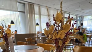 Een ontbijttafel met borden vol roerei, toast en een plakje cake, plus een vaas gedroogde bloemen.