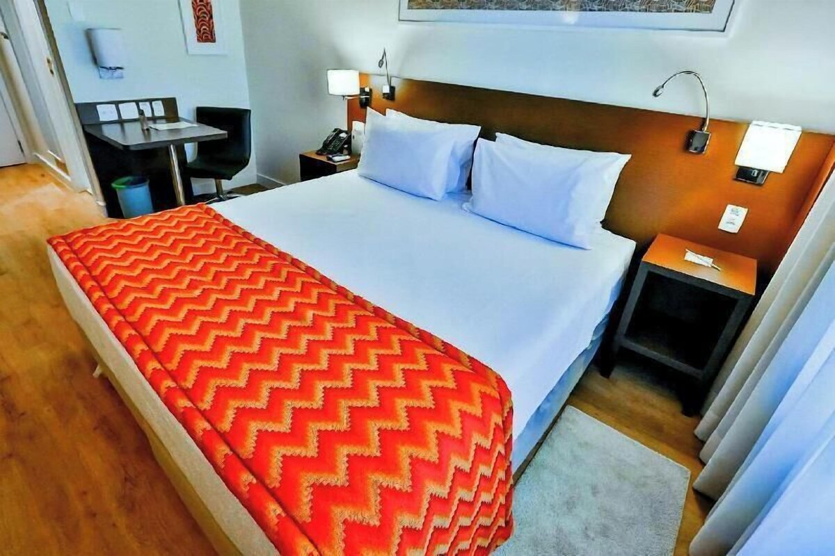 Een hotelkamer met een bed, een bureau, een stoel, een nachtkastje en een lamp.