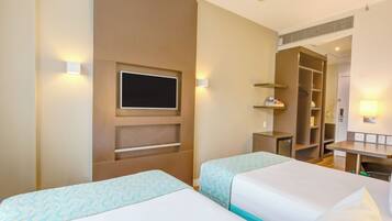 A hotel room with two beds, a TV mounted on the wall, a desk with a chair, and a wardrobe.