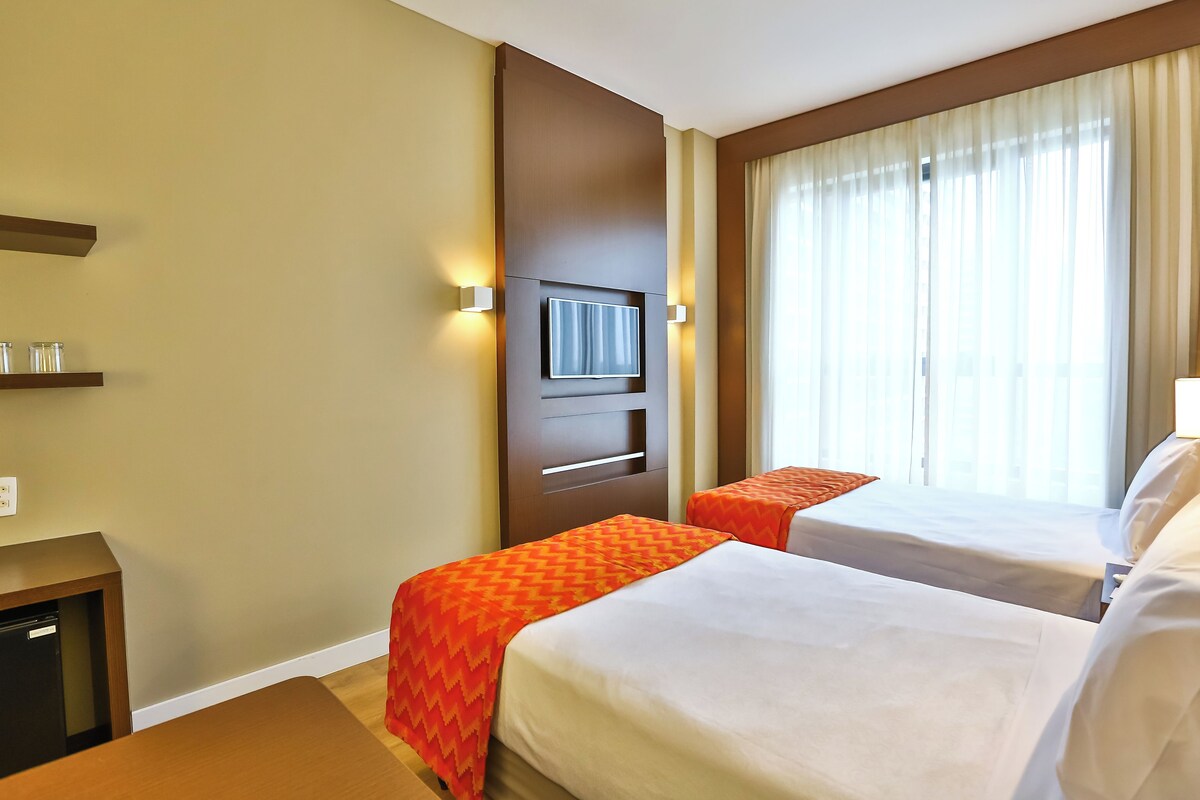 Een hotelkamer met twee bedden, een televisie, een minibar en een raam met gordijnen.