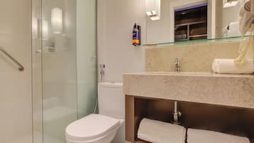 A modern bathroom with a glass shower enclosure, a white toilet, a beige countertop with a sink, and a mirror above the sink.