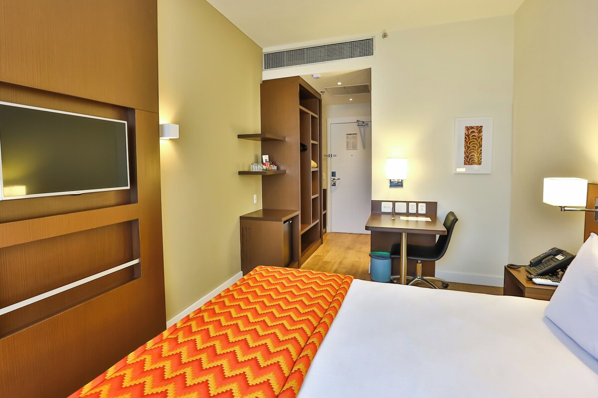 Hotelkamer met een bed, bureau met stoel, televisie aan de wand en een kledingkast.