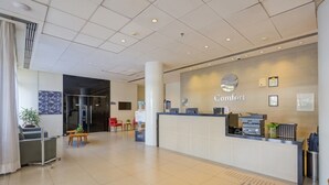 Een modern ingerichte hotelreceptie, met een receptiebalie, zithoek en een grote potplant.