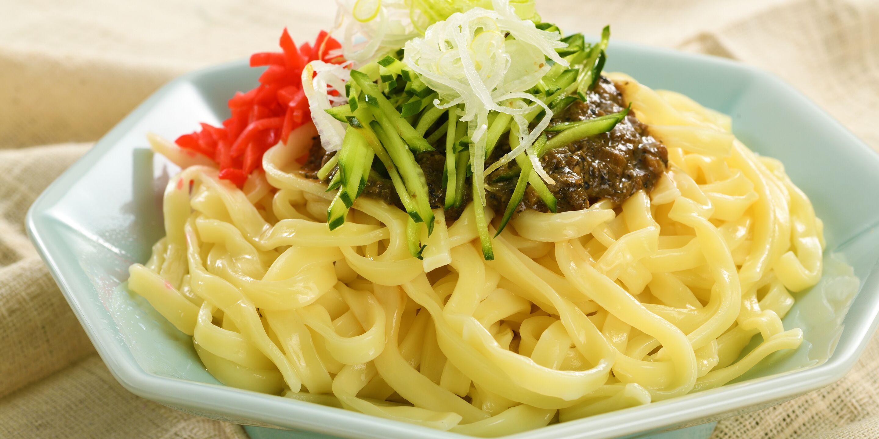 Un plato de fideos cubierto con vegetales verdes y salsa oscura.