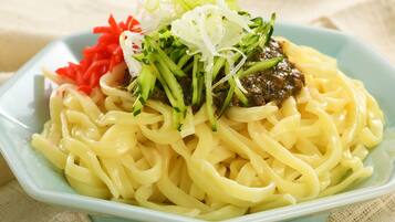 Un plato de fideos cubierto con vegetales verdes y salsa oscura.