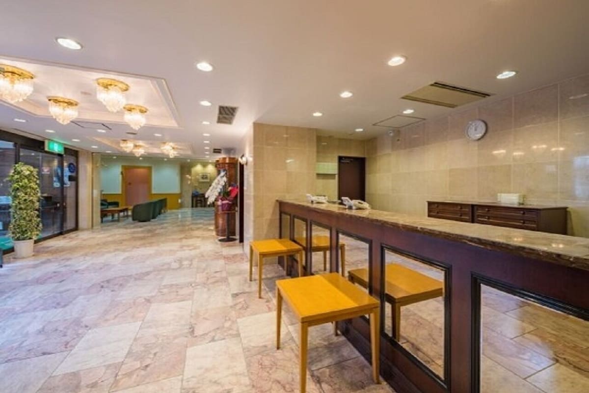 Un hall d’hôtel avec un sol en marbre, un comptoir d’accueil doté de tabourets de bar et une horloge murale.