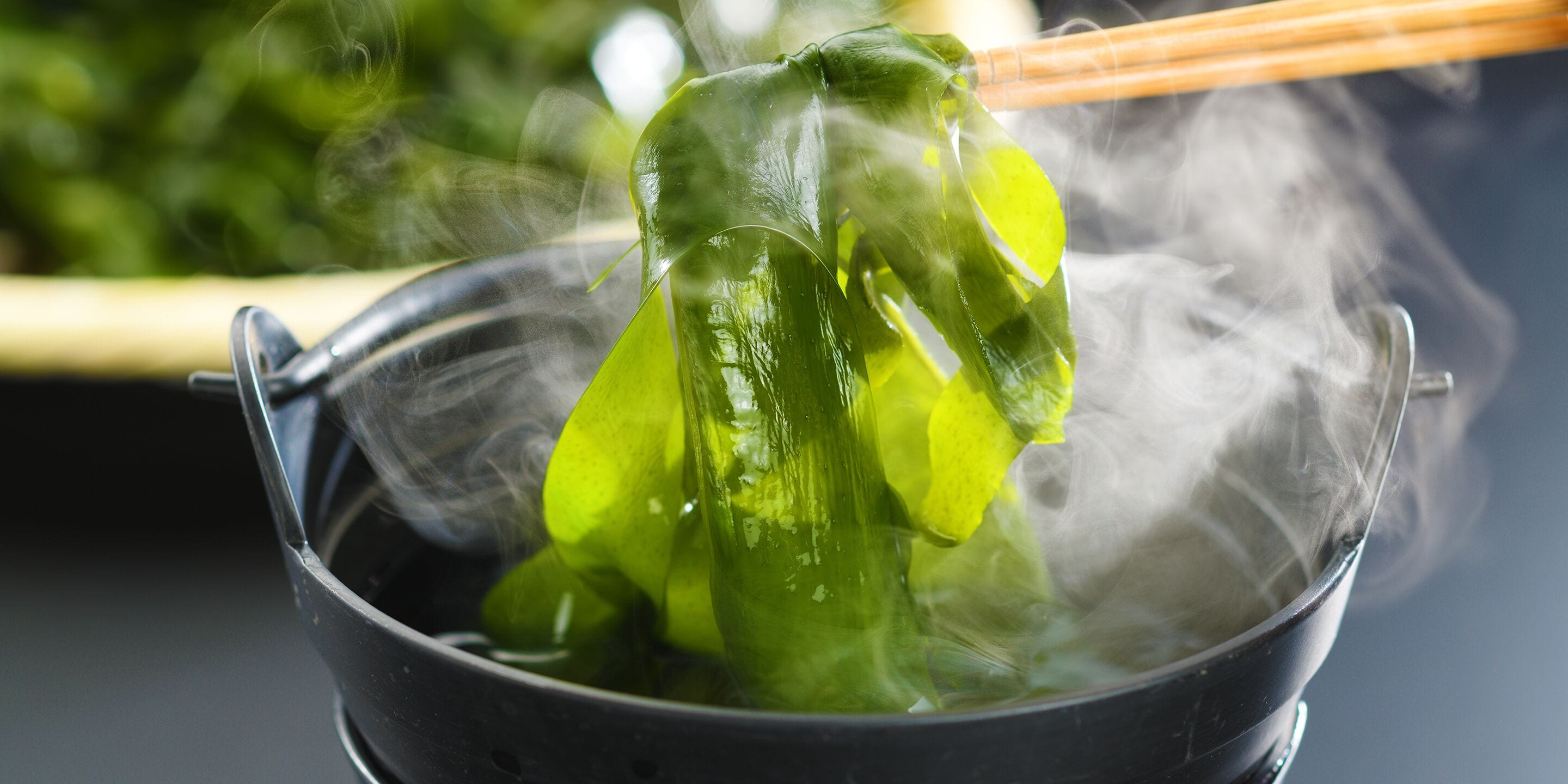 Un tazón humeante de verduras verdes con palillos.