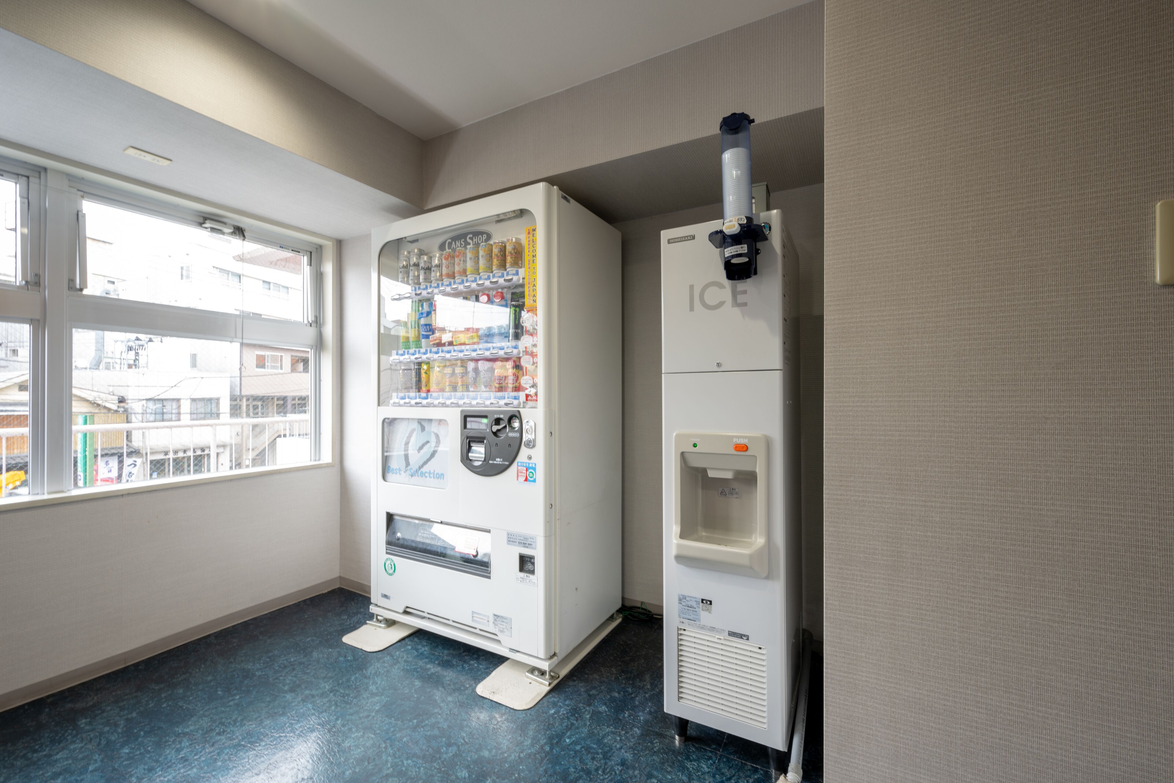 Un distributeur automatique équipé d’un point d’eau et d’un espace de sélection de boissons, situé dans une pièce dotée d’une grande fenêtre et d’un sol bleu.