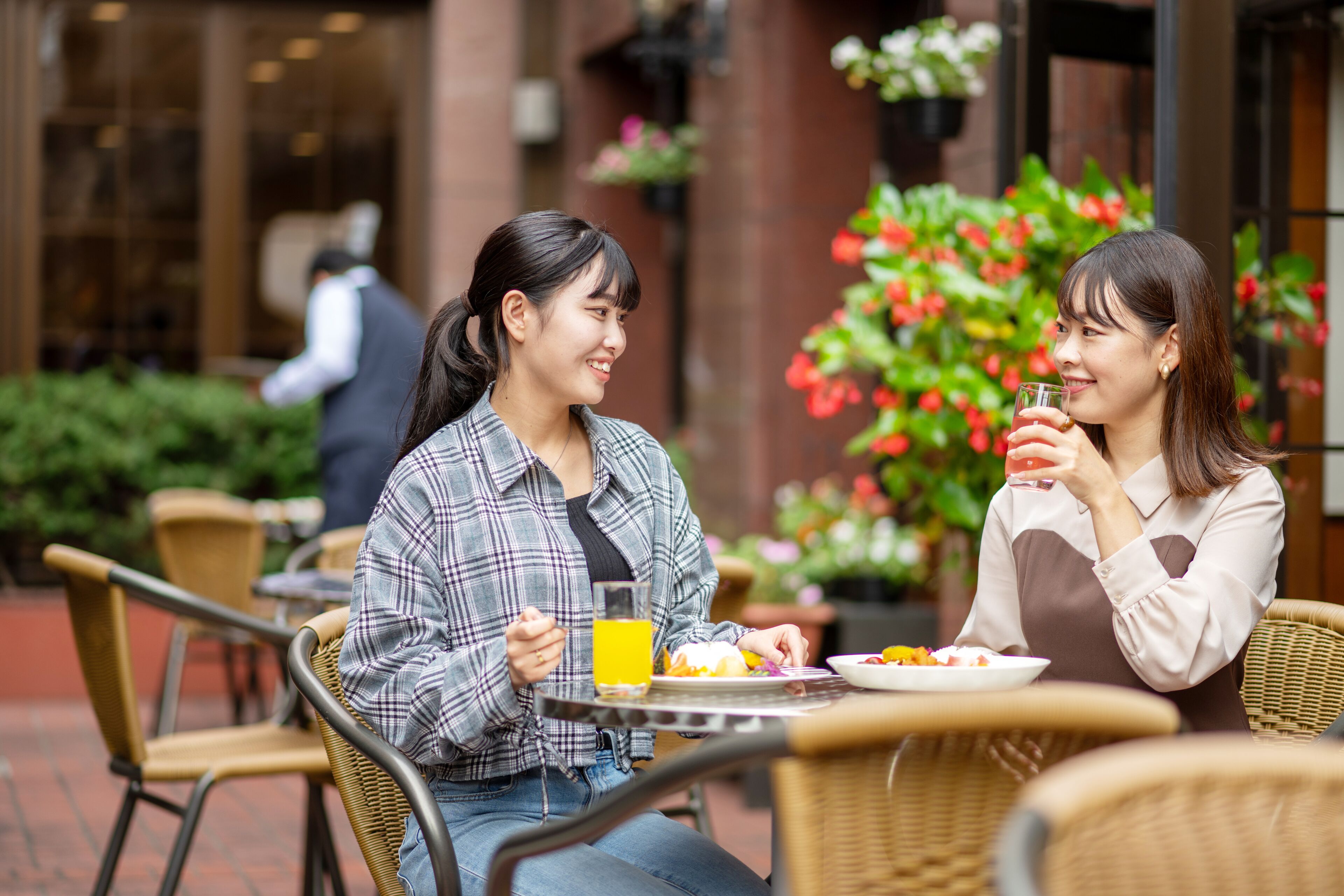 Two people dining at an outdoor cafe with wicker chairs and a brick floor.
