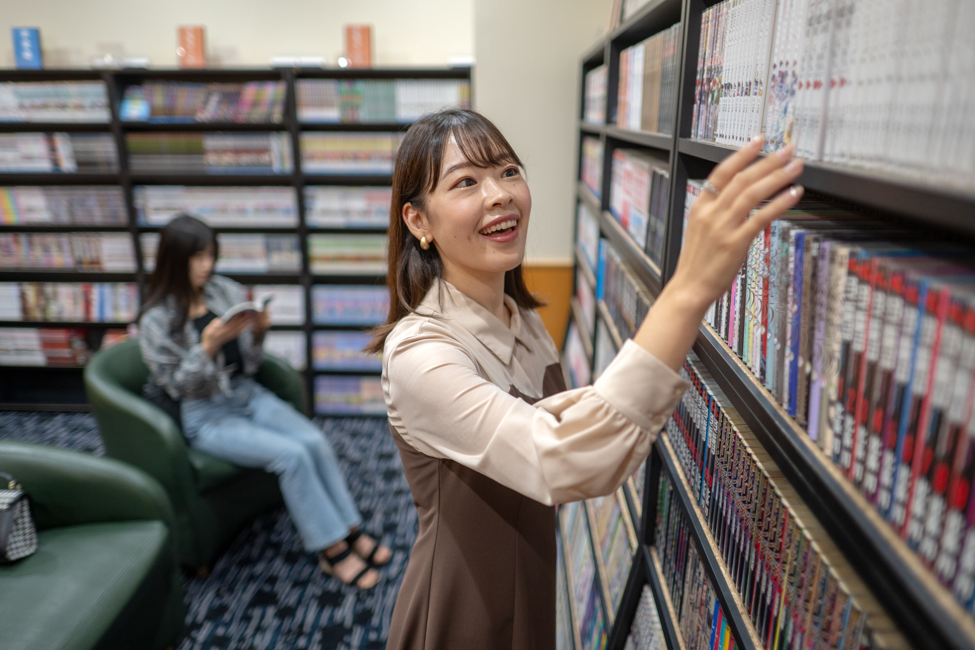 Una persona hojeando libros en una biblioteca, con estanterías y un sofá verde al fondo.
