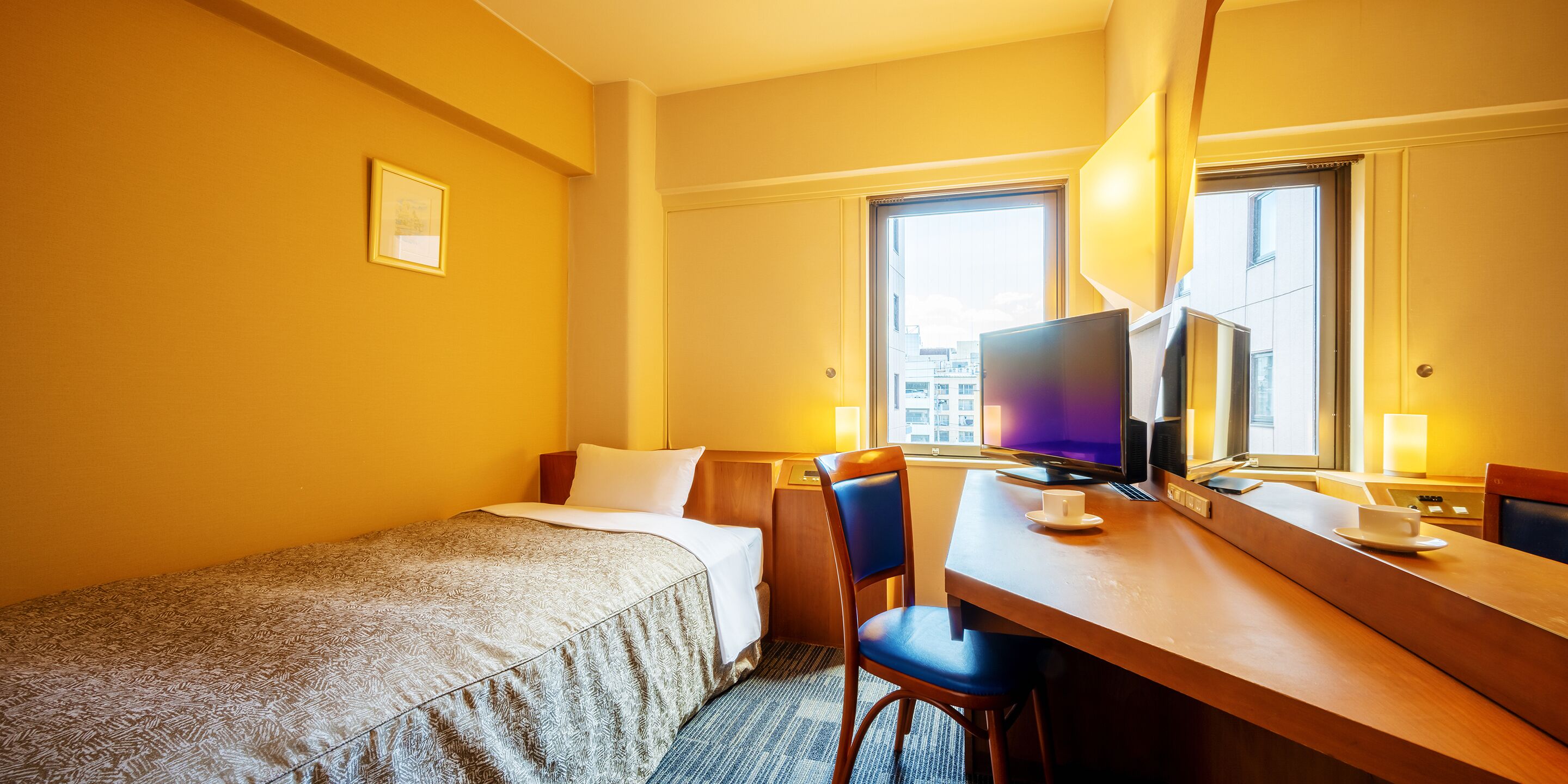 A hotel room with a single bed, a desk with a computer, and a chair.