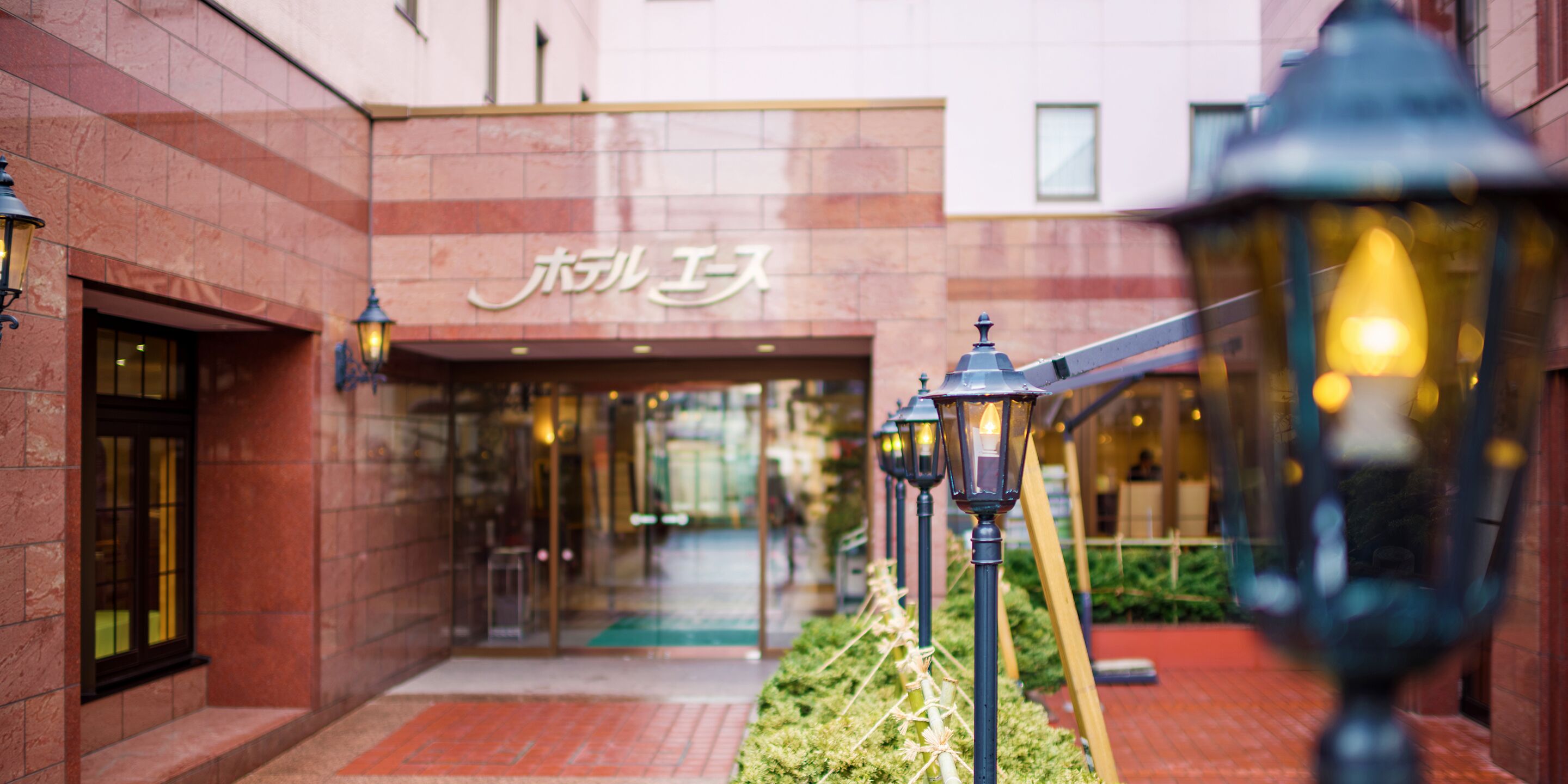 A building entrance with a sign, a pathway, and street lamps.