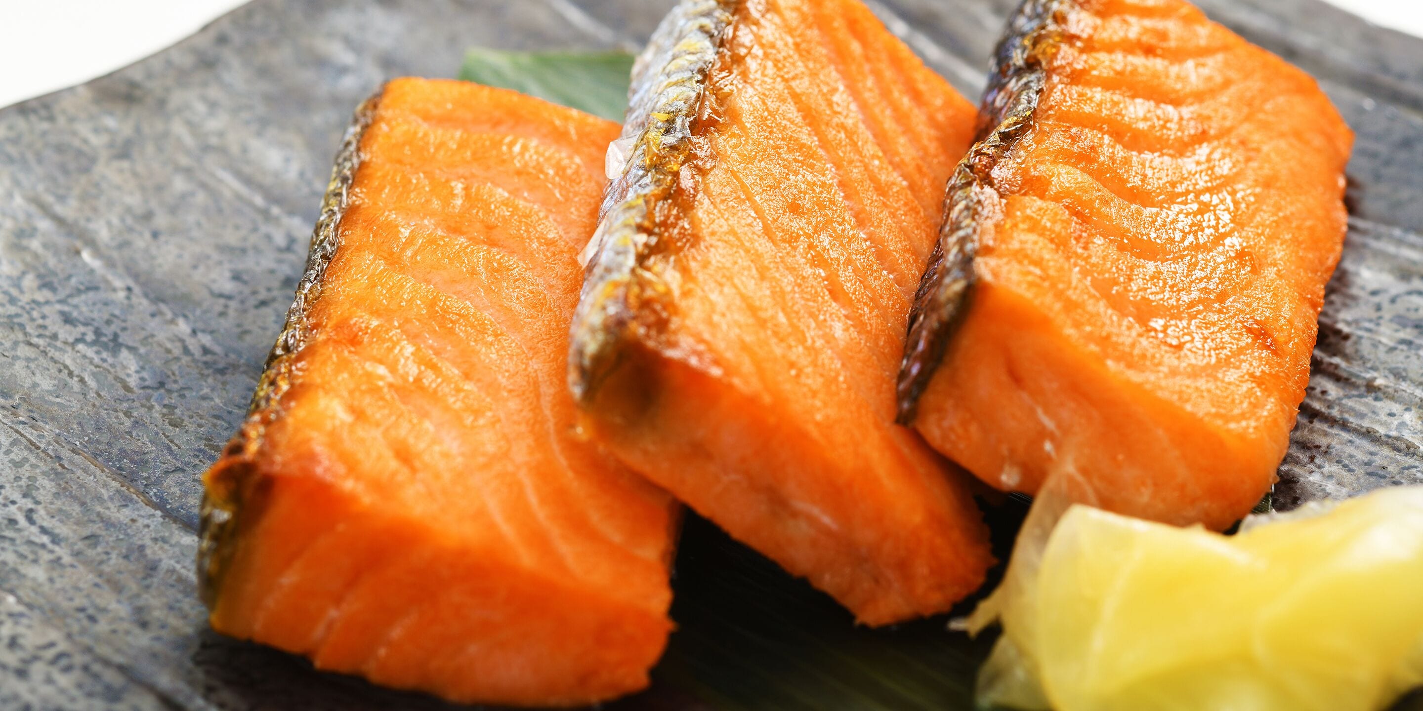 Three pieces of salmon on a dark slate plate with a lemon wedge.