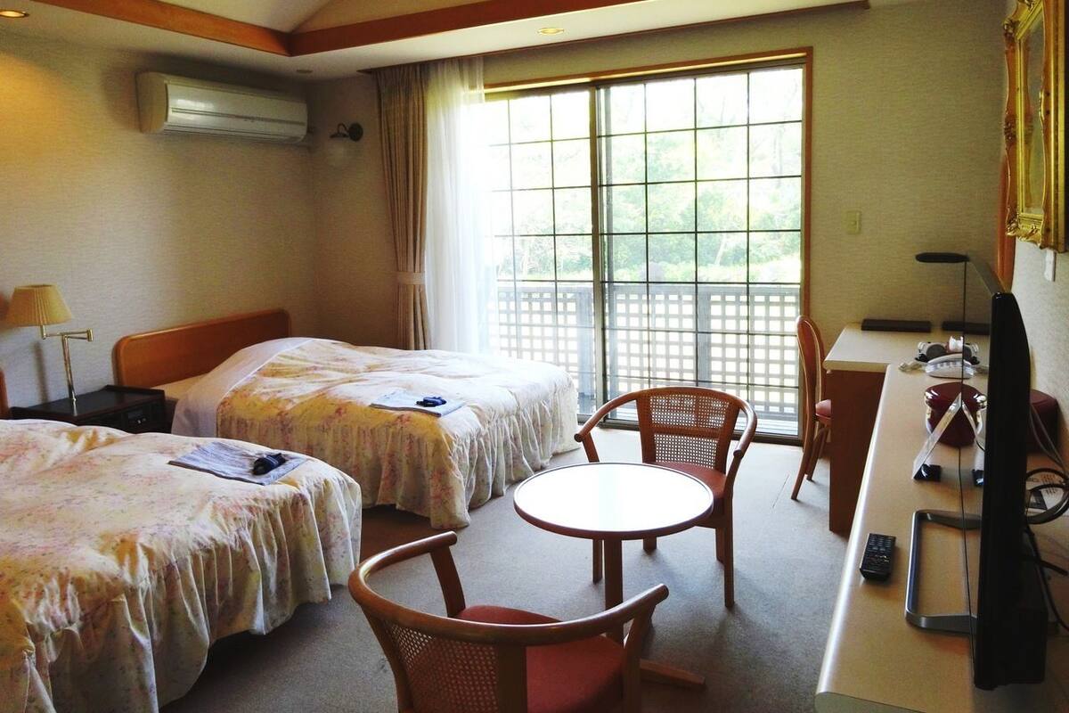 A hotel room with two beds, a desk, a chair, and a TV.