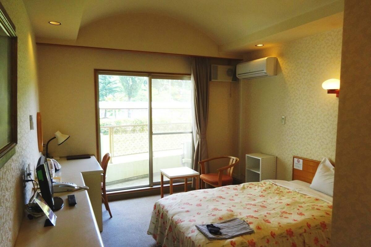 A hotel room with a bed, desk, chair, and a window with curtains.