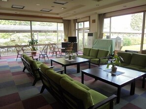 A hotel lobby with green sofas, a coffee table, and a TV. There are large windows with a view of greenery outside. - Hotel Kosaka Gold Palace (Kosaka)