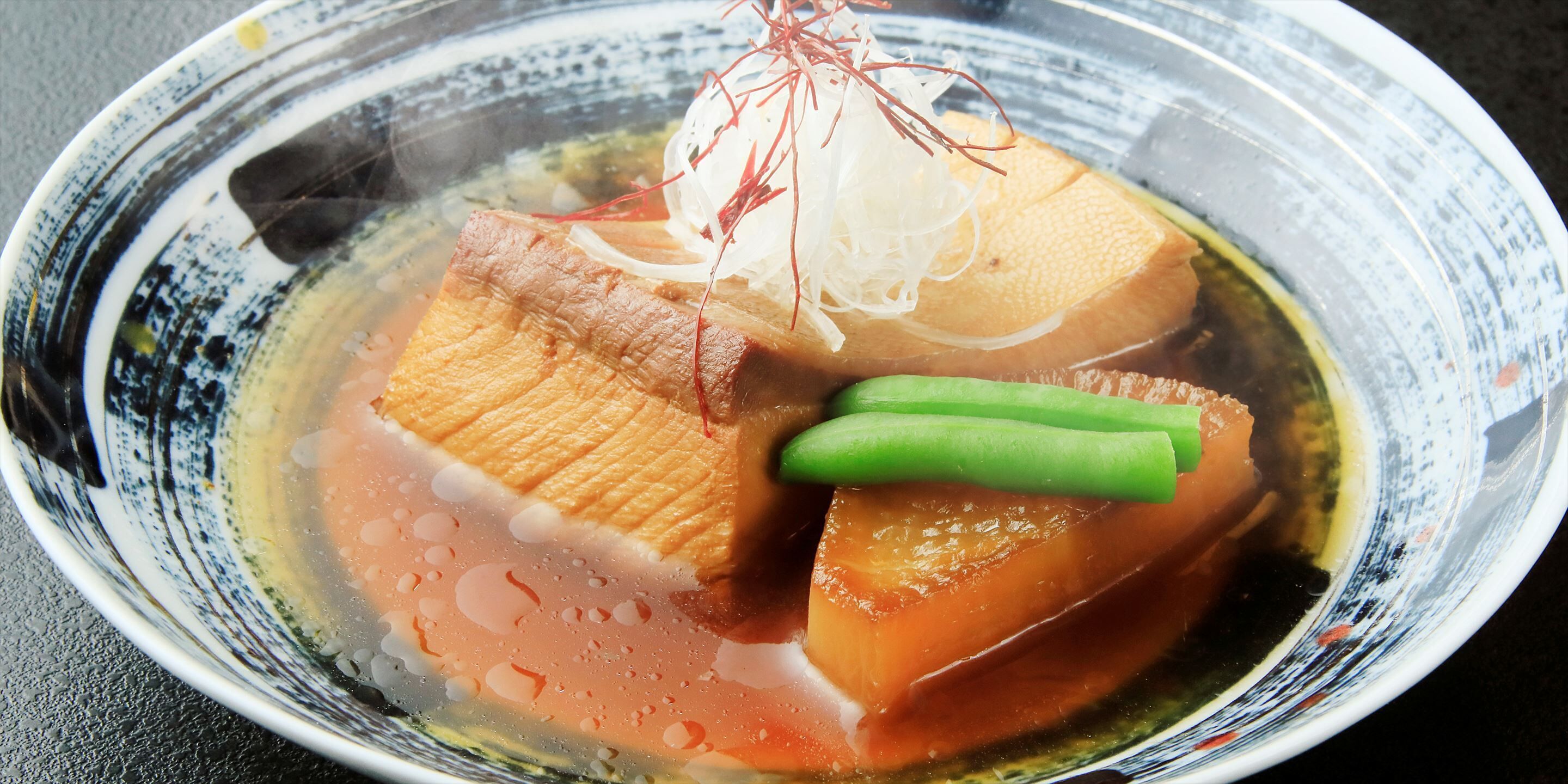 A bowl of sashimi with a clear broth, garnished with green vegetables and a red garnish.