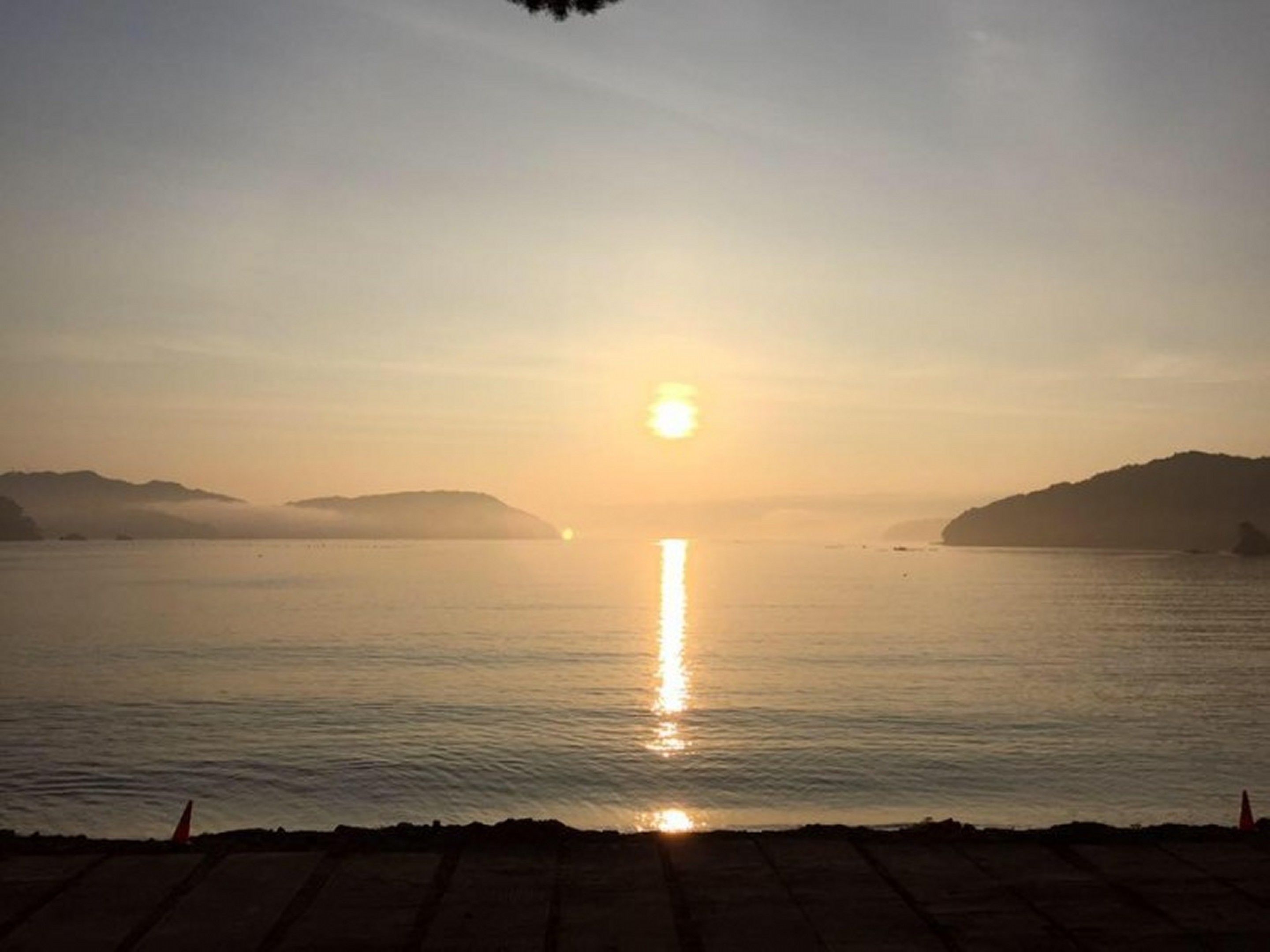 A sunrise over a calm body of water with distant landforms.