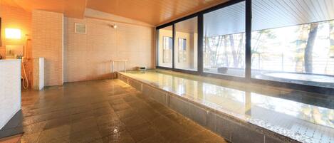 A modern indoor pool area with tiled flooring, a bench, and large windows offering views of the outdoors.