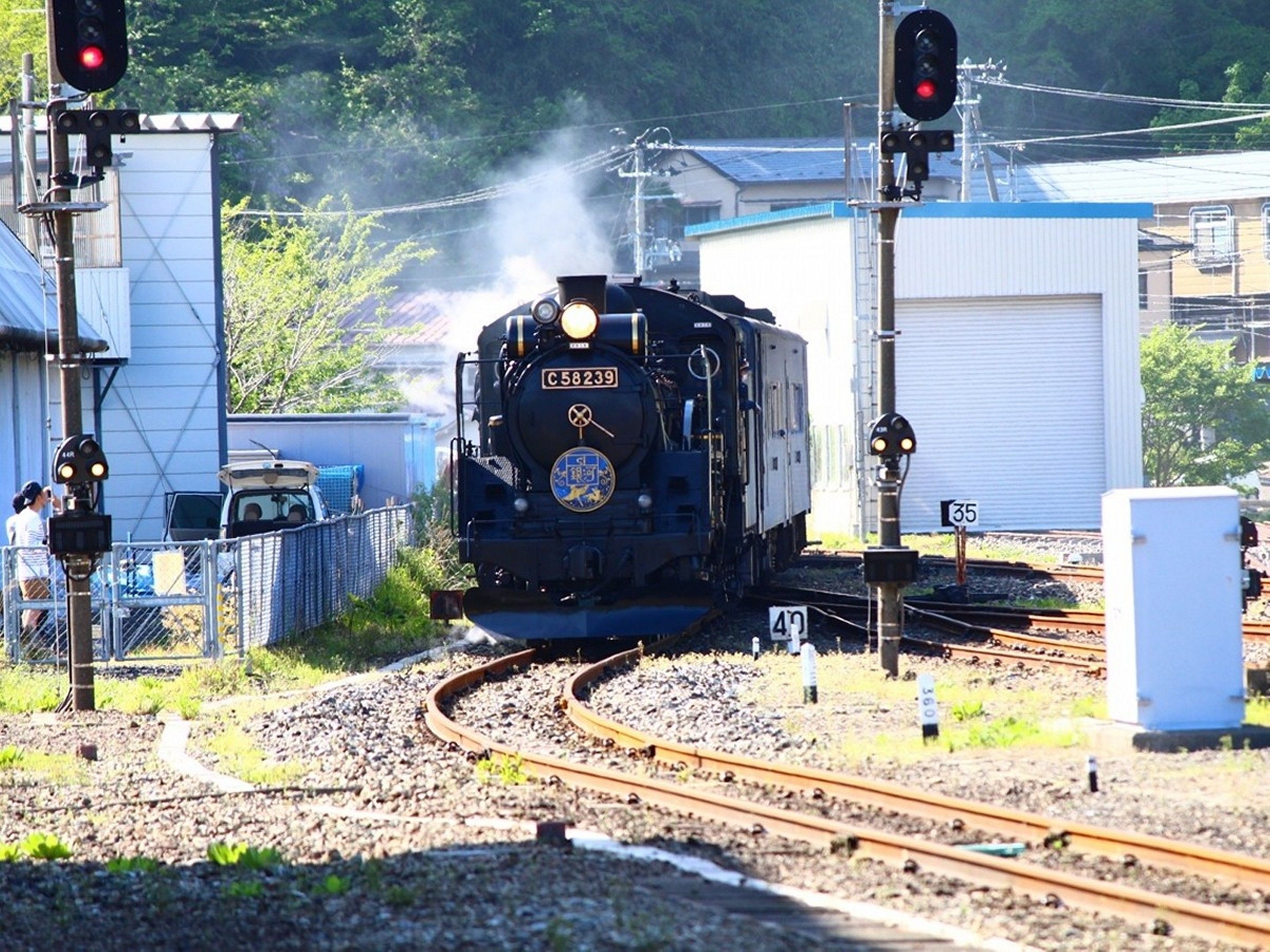 Ein Zug auf Gleisen mit der Nummernschild C58239 durchfährt einen Bahnübergang mit Signallampen und einem nahegelegenen Gebäude.
