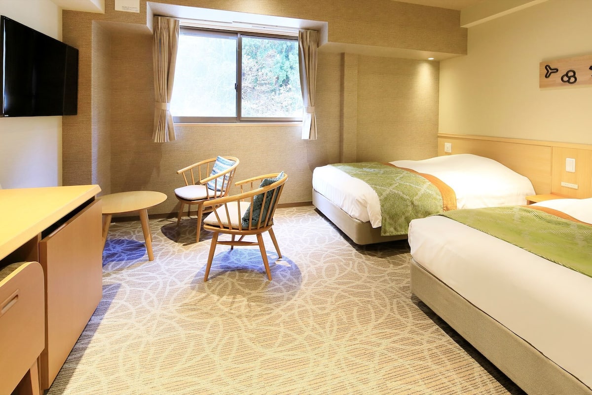 A hotel room with a bed, a desk, a chair, a TV, and a window.