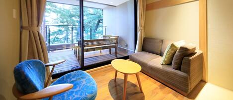 A modern living room with a sofa, two chairs, and a small table. A balcony with a bench is visible through the glass doors.