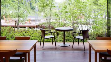 Un patio con mesas y sillas de madera, rodeado de abundante vegetación y vistas a la calle.