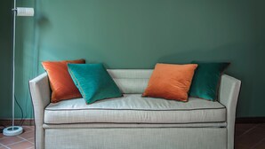 A beige sofa with two orange and two teal cushions against a green wall. - Brera Apartments in Porta Romana (Milan)